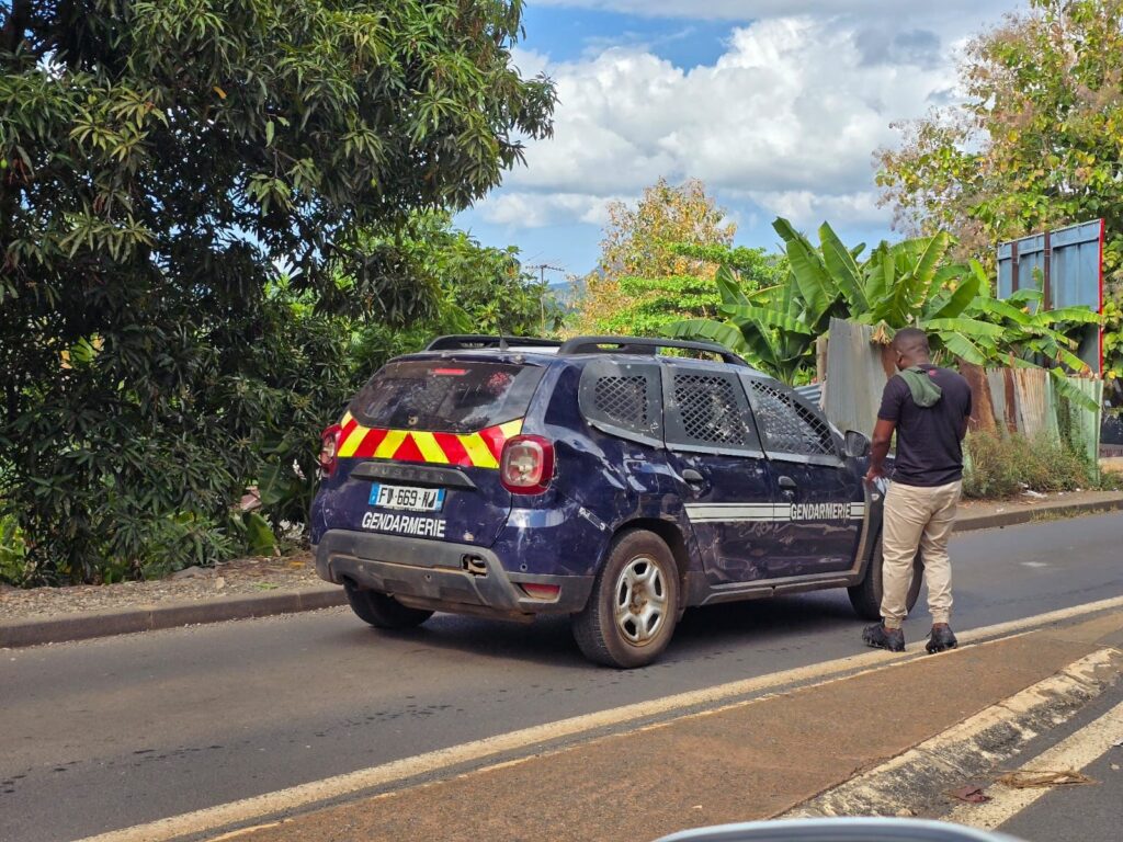 Patrouille de gendarmerie circulant dans une zone urbaine de Mayotte, avec tensions locales et intervention des forces de l’ordre pour disperser un groupe.